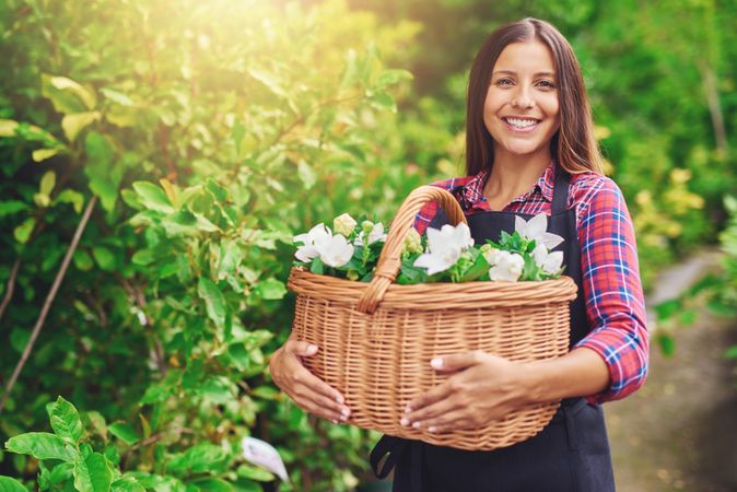 Confident smiling woman pictured in a greenhouse holding a basket of flowers