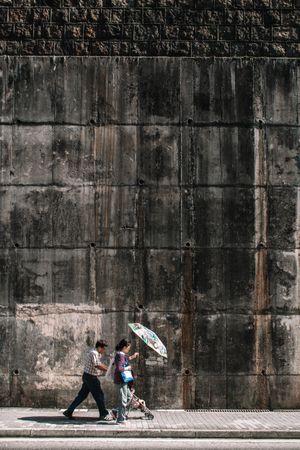 Side view of two people walking on sidewalk beside an ancient gray wall