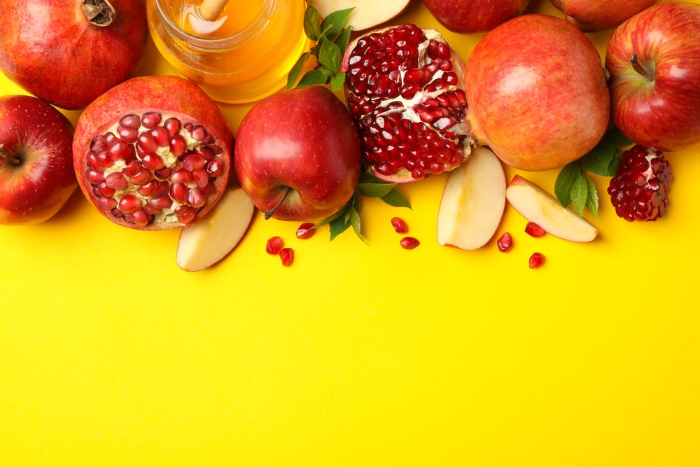 Top view of fresh apples, pomegranate and honey on yellow background with copy space