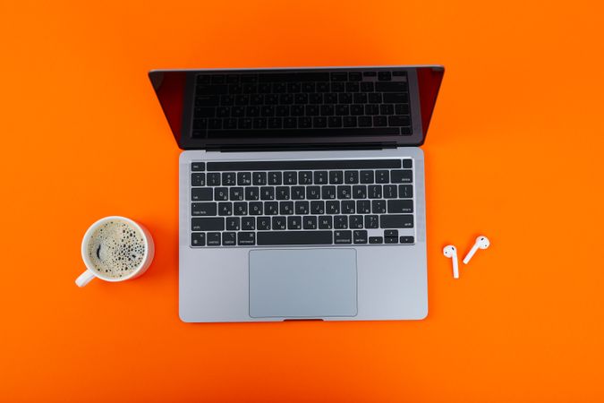 Looking down at laptop on orange desk with mug of coffee or tea and ear buds