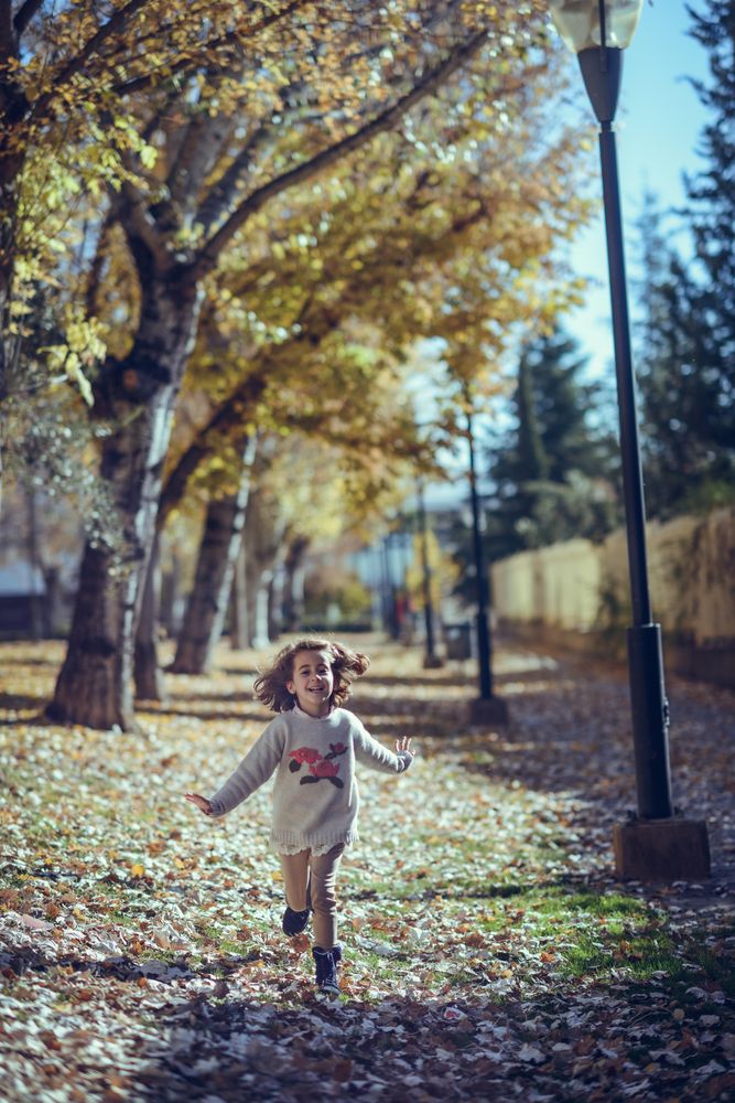 Happy child running in park of colorful fall leaves