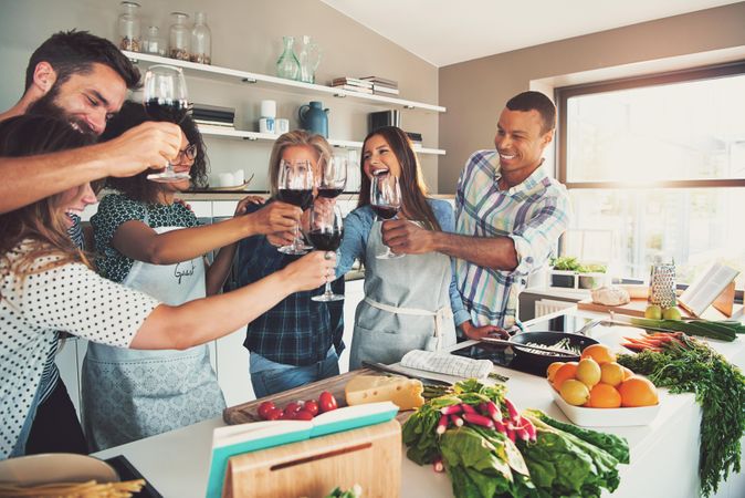 Multiethnic friends toasting red wine while cooking in a bright kitchen