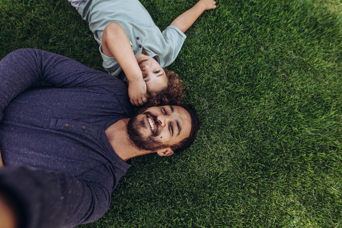 Man lying on grass in a park with his son