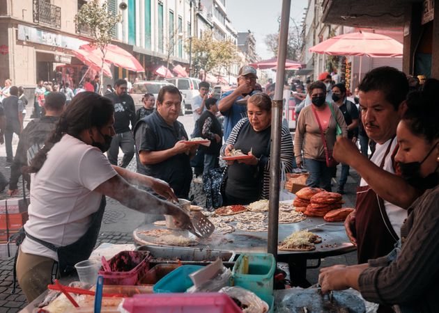 Group of people standing around as tacos are cooked on outdoor grill