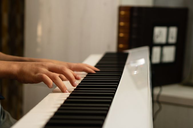Boy’s hands playing a white digital piano.