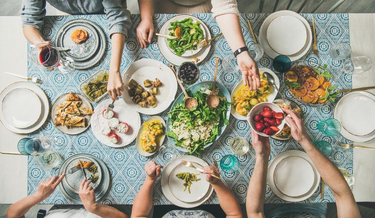 Group of people at blue patterned table with fresh fruits, salad, and vegetables