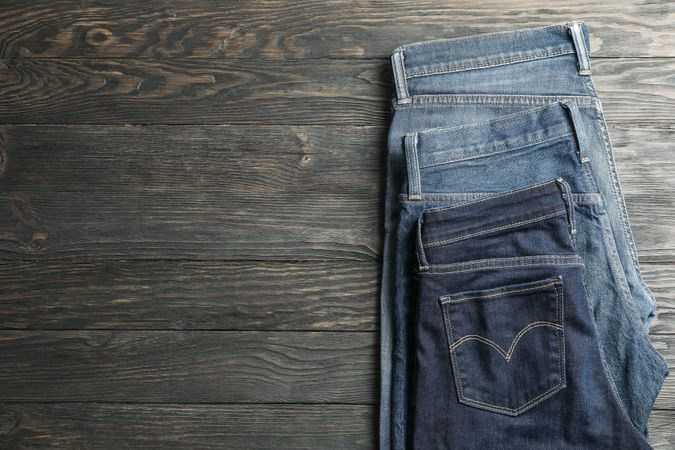 Different jeans folded on a wooden background, space for text