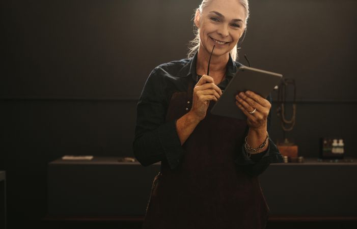 Portrait of smiling woman wearing apron holding digital tablet in her jewelry workshop