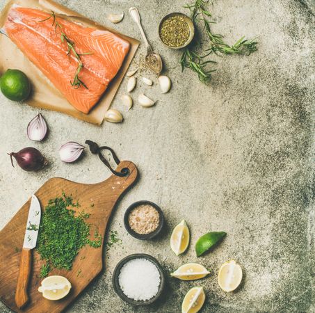 Salmon fillet with fresh herbs, limes, onions, bread board, square crop, copy space