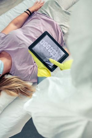 Top view of unrecognizable female doctor in protective suit examining x-ray of patient on tablet