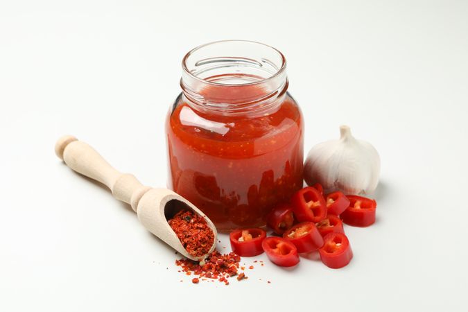 Chilli, garlic, spice and jar with sauce on plain background