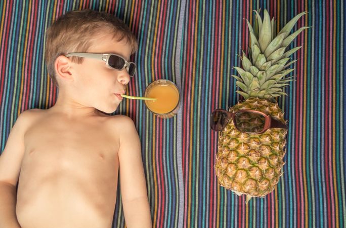 Happy child and pineapple sunbathing over a towel