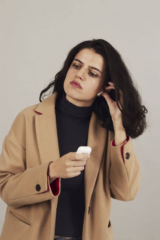 Serious young woman putting on earbuds in studio