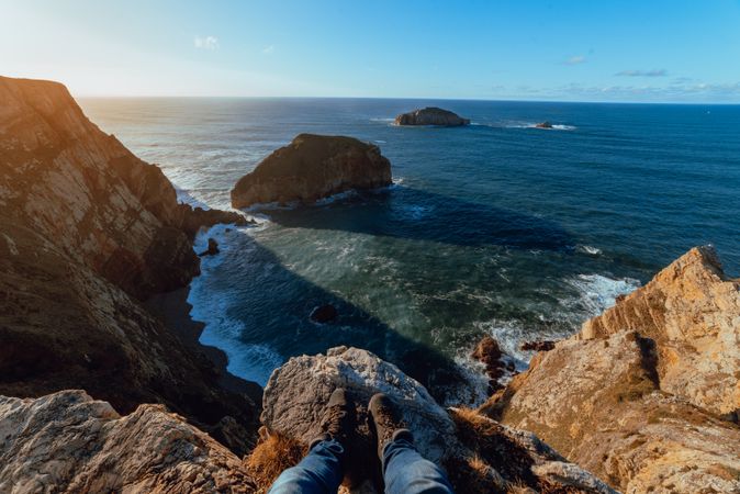 Person sitting on cliff near water