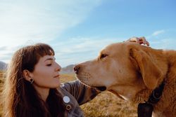 Woman with piercing sitting near dog between field
