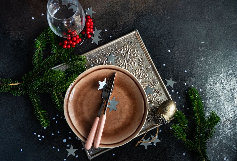 Rustic plate with cutlery and glass surrounded by wintry pine and star ornaments