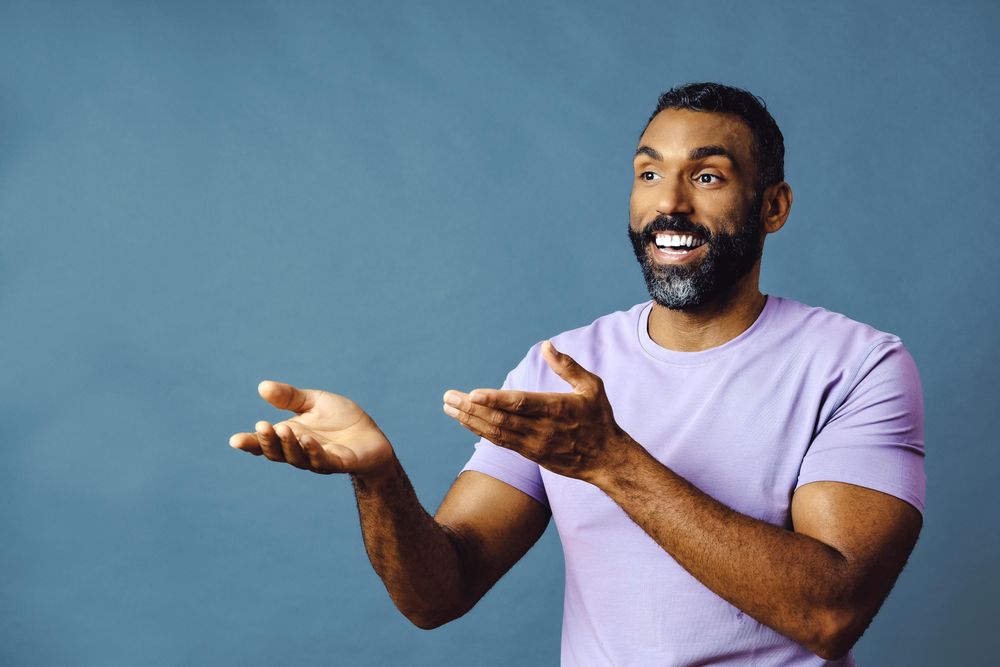 Male speaking in purple t-shirt with hands gesturing to copy space