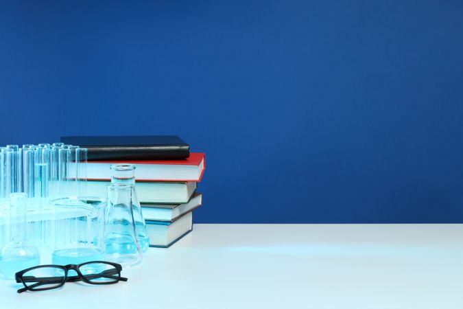Books, flasks and glasses on blue background, space for text