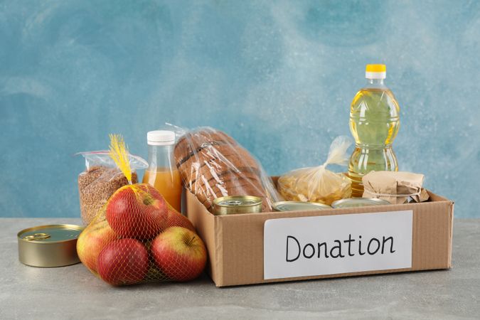 Donation box with different food on gray table. Volunteering