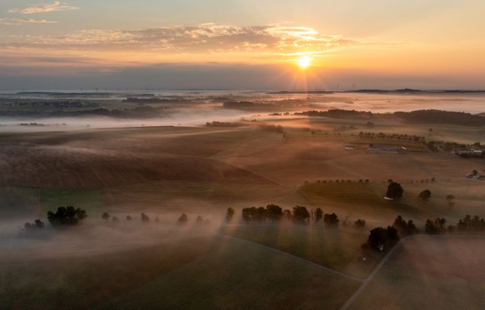 Drone aerial view of agricultural fields covered in fog at golden hour