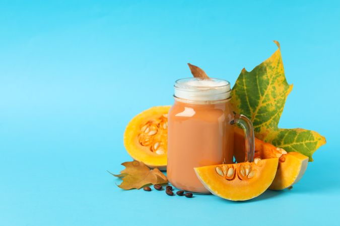 Composition with glass jar of pumpkin latte on blue background