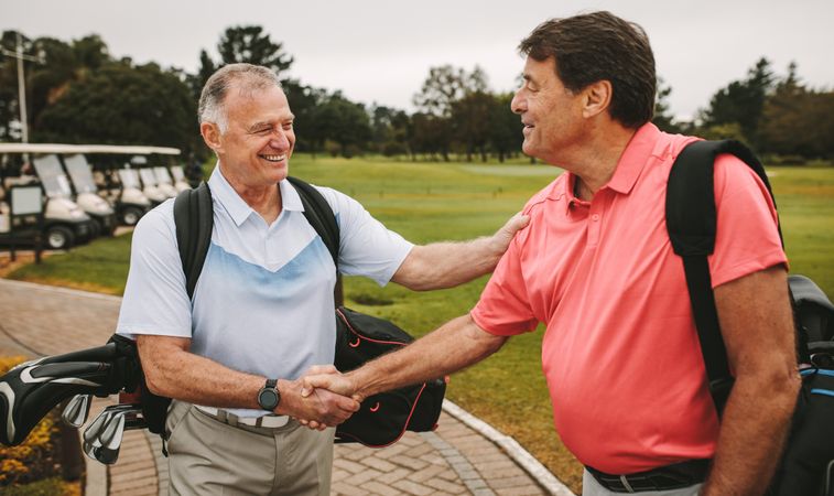 Happy mature men are shaking hands and smiling when meeting on a golf course