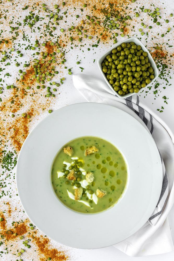 Green vegetable cream soup with crackers and peas in bowl