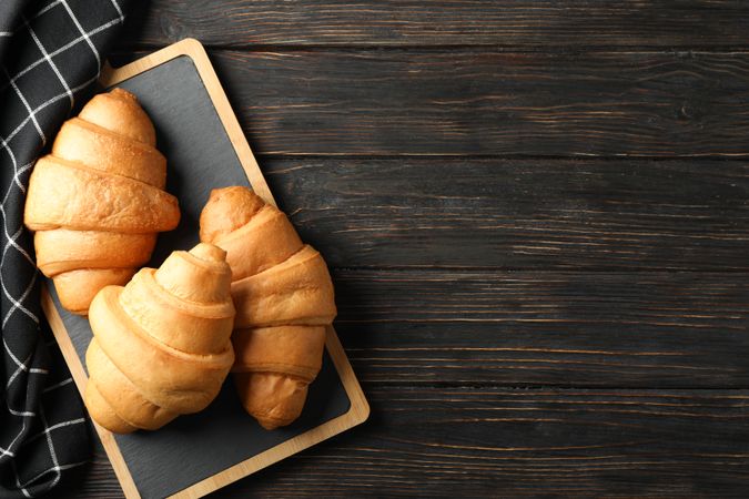 Bread board with croissants on table with kitchen towel, top view with copy space