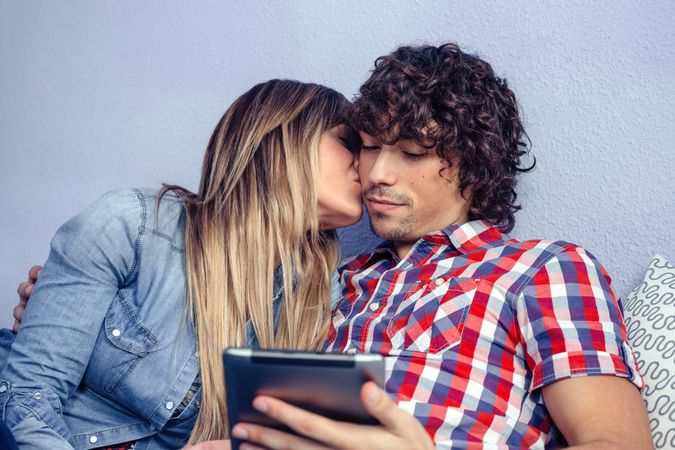 Woman kissing man looking at tablet