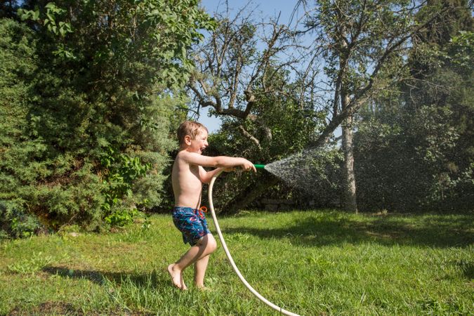 Little child having fun with garden hose and water