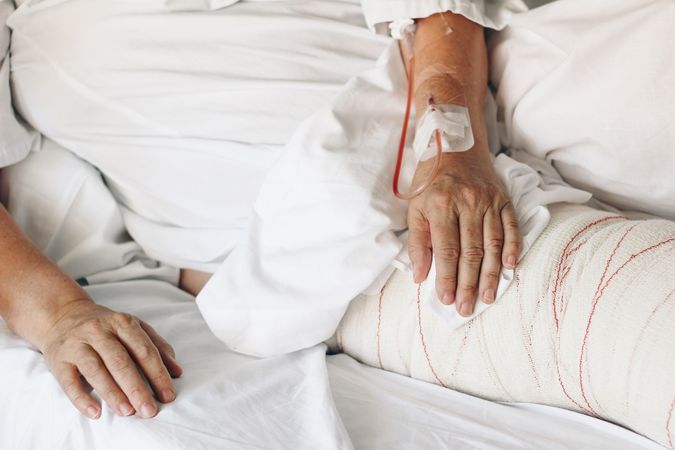 Closeup of hands with vein cannula and bandaged leg