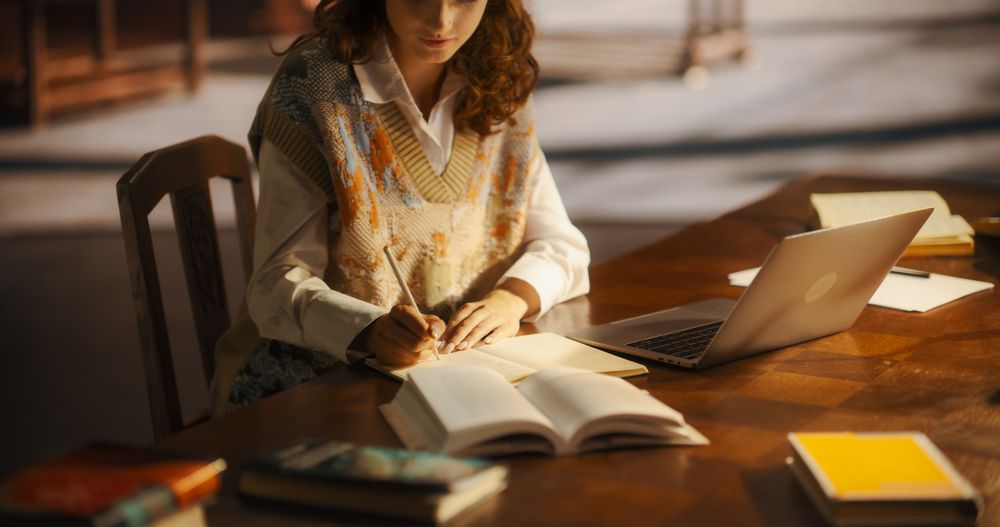 Dedicated Young Woman Engaged in Academic Research With Books and Laptop in a Cozy Library Setting