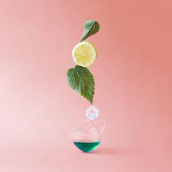 Deconstructed nettle tea with leaves, lemon slice, mug, ice on pink background