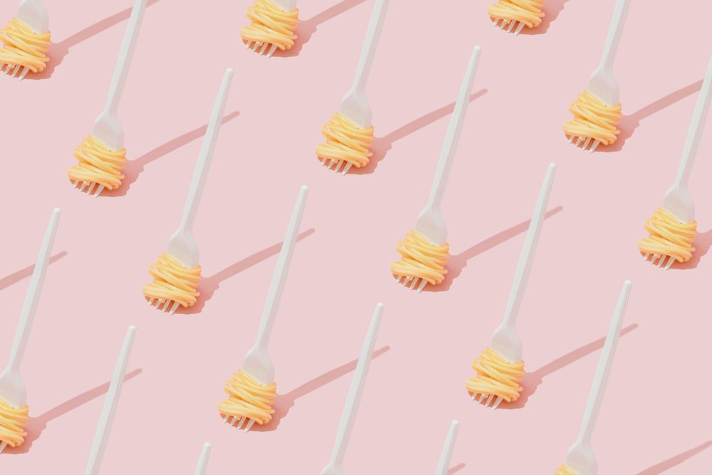 Rows of plastic fork with pasta pattern against pastel pink background
