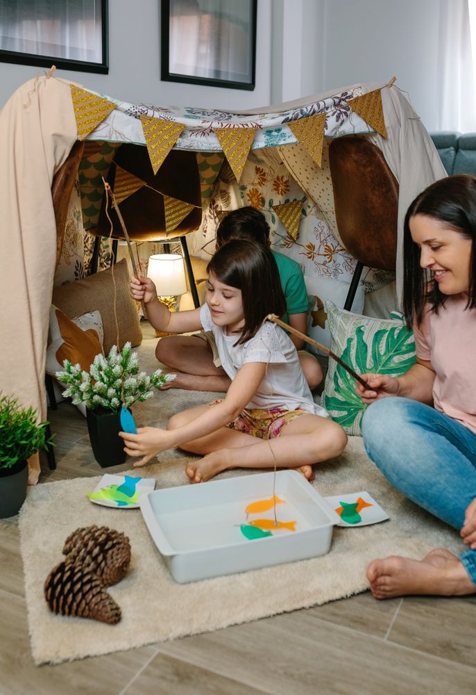 Happy mother and daughter camping at home playing diy fishing game