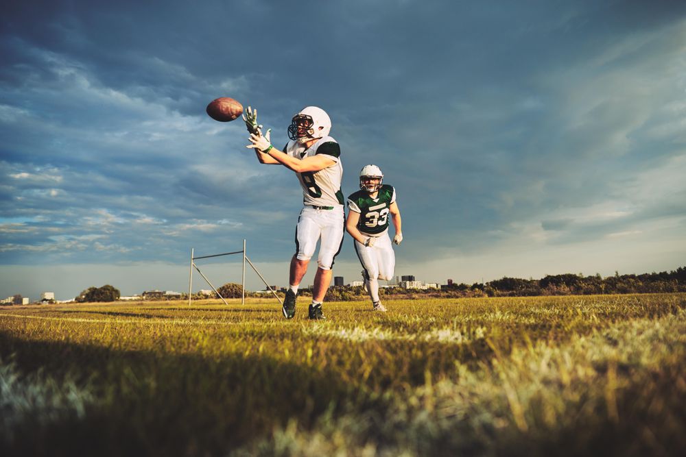 Man catching football midair with team mate running alongside