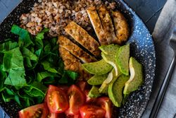 Looking down at healthy fresh meal with avocado, grains, tomatoes & spinach