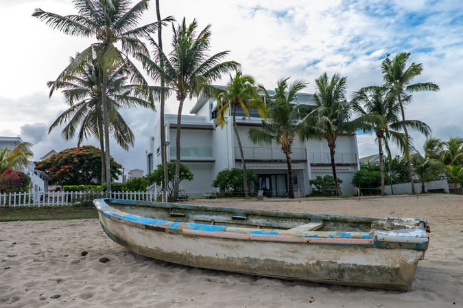 Old boat on sand in front of house and palm trees