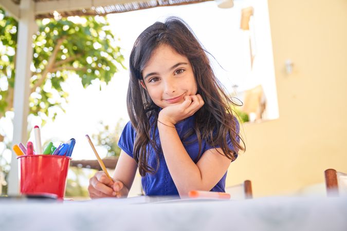 Charming girl sitting at table and drawing picture