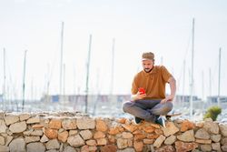 Man in cap relaxed sitting on skateboard using mobile phone