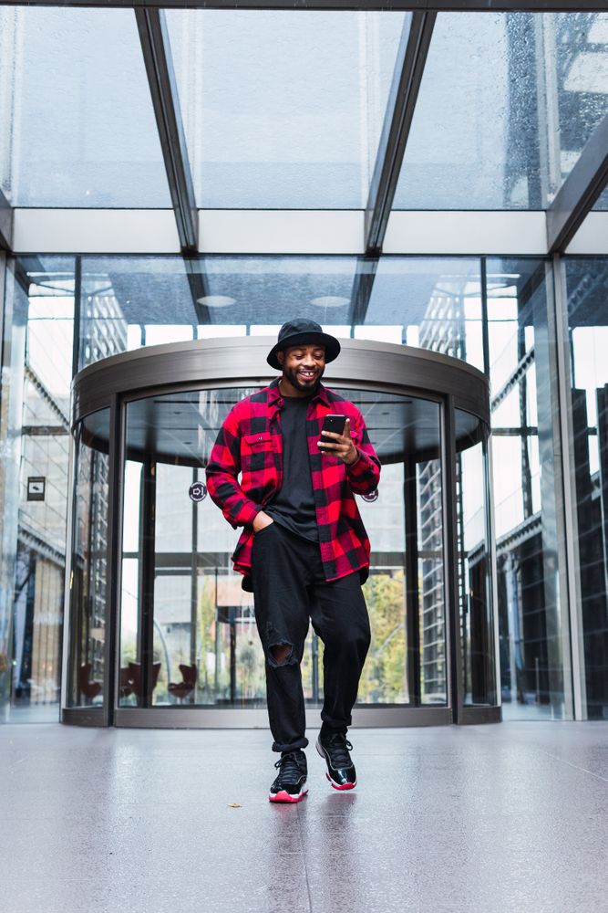 Cheerful Black male with smartphone in contemporary building