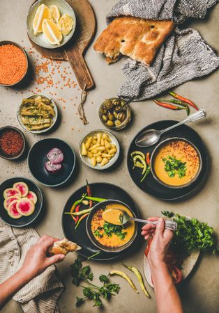 Spread of yellow lentil soup bowls, with bread, vegetable garnishes with man with spoon in soup