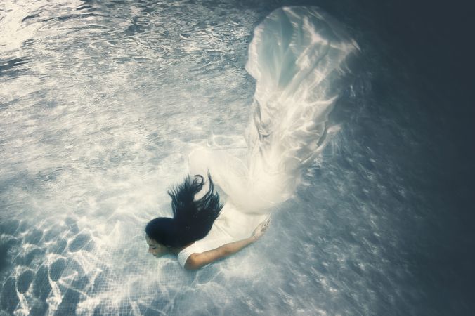 Woman in wedding dress floating underwater