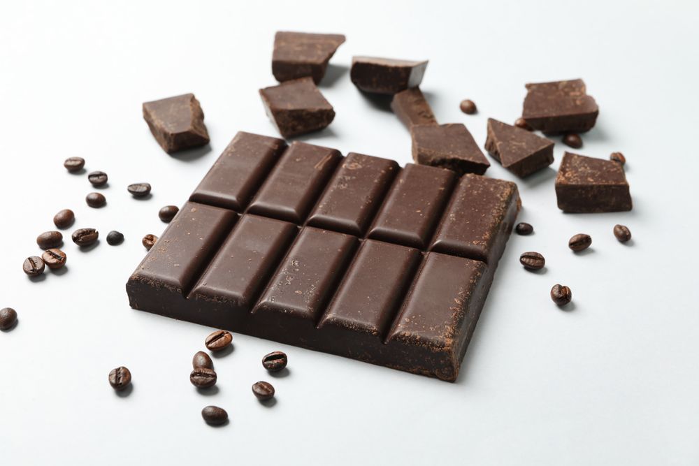 Chocolate bar and coffee seeds on light background
