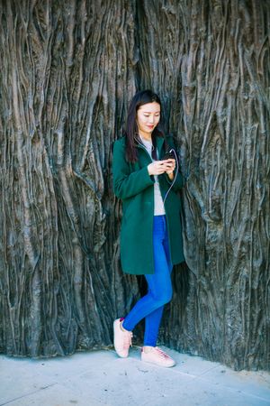 Asian female listening to music near rough wall