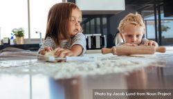 Little boy using rolling pin and girl kneading dough with flour on kitchen table 0g7Rl0