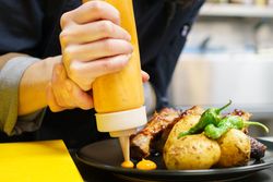 Hand squeezing sauce onto restaurant dish