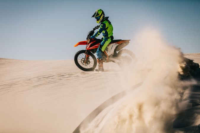 Dirt biker speeding over sand dunes