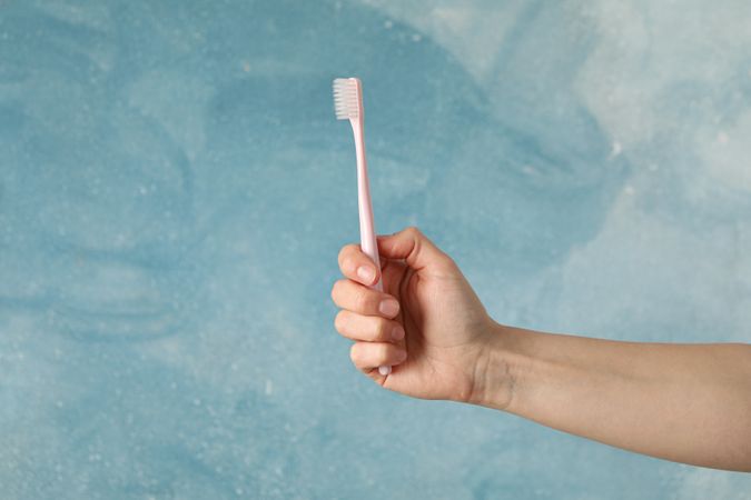 Female hand holds toothbrush on blue background. Oral care