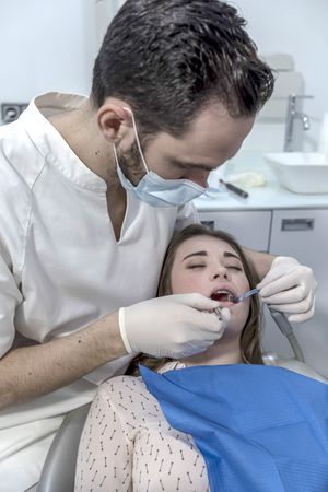 A portrait of a dentist examining female mouth, vertical